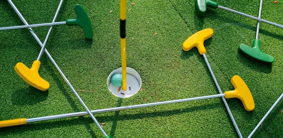 mini golf clubs laid around a ball inside a hole
