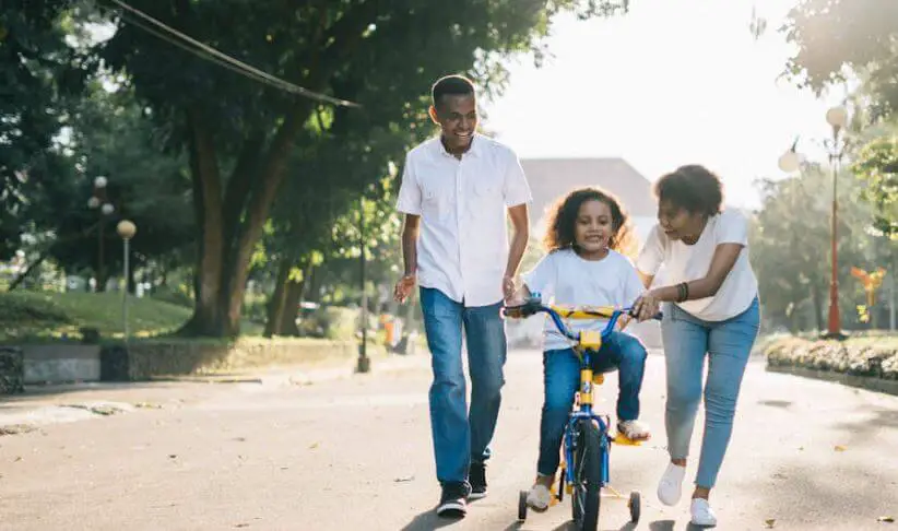 parents helping child ride a bicycle